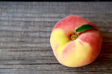 Chinese flat peach with leaves on old wooden table.Donut peach also known as Saturn peach,Paraguayo,Pan tao,Saucer peach,Belly-up peach,UFO peach or Hat peach.