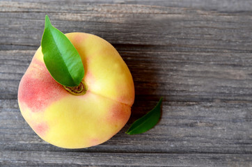 Chinese flat peach with leaves on old wooden table.Donut peach also known as Saturn peach,Paraguayo,Pan tao,Saucer peach,Belly-up peach,UFO peach or Hat peach.