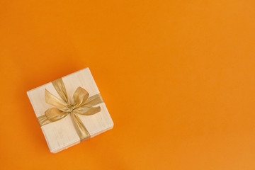 White gift or present box decorated with golden ribbon on orange background. Top view, copy space. Holiday concept