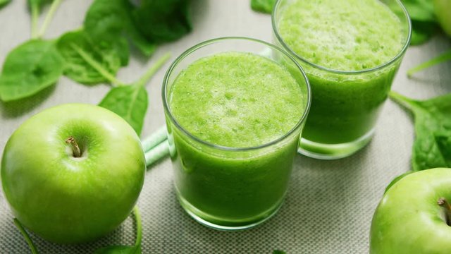 From above shot of glasses filled with green smoothie on table with spinach leaves and apples 