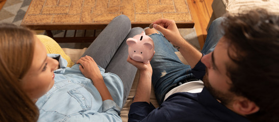 Happy couple inserting coin in piggybank