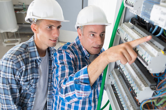 journeyman and apprentice electrician working to repair a circuit panel