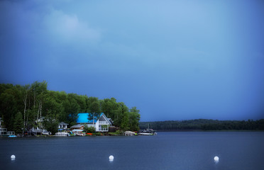 Middle class homes along a calm lakefront with green trees in the baclground under an ominous blue sky on a cloudy afternoon summer landscape