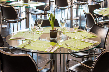 Glasses, flower, fork, knife served for dinner in restaurant with cozy interior.