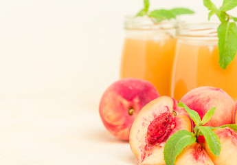 Peach smoothie in glass jars with fresh ripe fruits and green mint leaves on yellow pastel background.