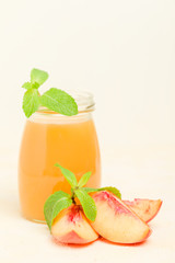 Peach smoothie in glass jars with fresh ripe fruits and green mint leaves on yellow pastel background.