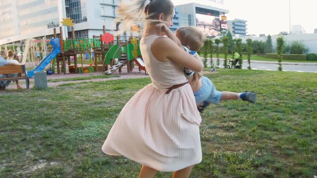 4k video of young mother holding and rotating her little toddler boy on playground at park