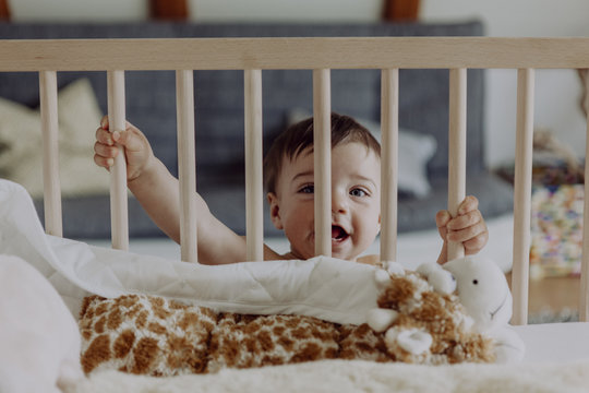Baby boy holding on to his cot laughing