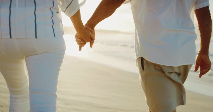 Middle age couple holding hands enjoying sunset walk