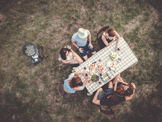 group of young people having a barbeque picnic in the garden sitting at the table drinking wine. the grill is prepared.
