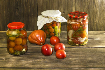 Food. Homemade canned vegetables in jars. Marinated tomatoes and cucumbers on the background of a wooden table in a rural style