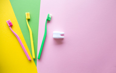 Plastic colorful toothbrushes and white tooth on a yellow, green, pink background. Dental care concept. Teeth care minimalism concept.