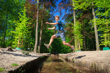 Mentally challenged, but nevertheless cheerful, individual takes a big leap (in life) and jumps over a small stream in the spring forest
