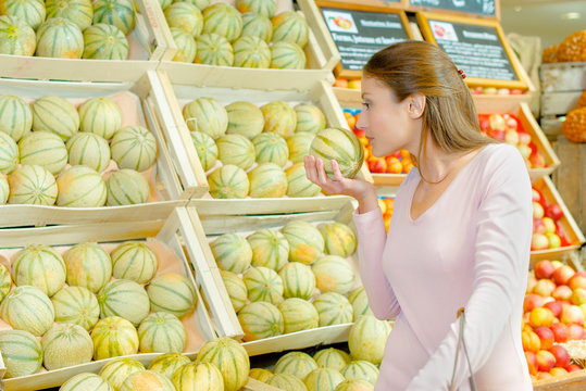 Lady smelling melon in grocers