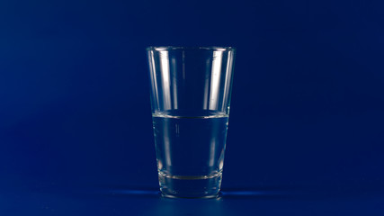 Glass with half of clear water on a blue background