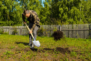 Young guy digs the ground in the garden with a shovel