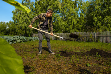 Young guy digs the ground in the garden with a shovel