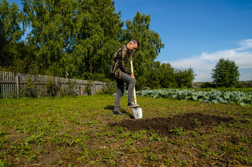 Young guy digs the ground in the garden with a shovel