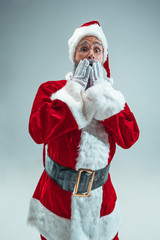 Funny surprised guy with christmas hat posing at studio. New Year Holiday. Christmas, x-mas, winter, gifts concept. Man wearing Santa Claus costume on gray. Copy space. Winter sales.