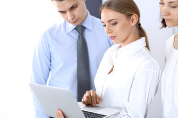 Obraz premium Group of business people using laptop computer while standing in office. Meeting and teamwork concept