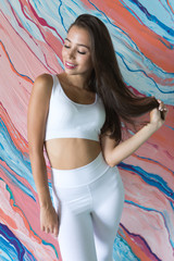 Attractive young woman in white sports top and leggings on a colored background.