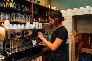 lateral view of beautiful girl bartender making a coffee at the espresso machine