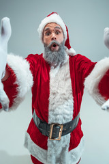 Funny surprised guy with christmas hat posing at studio. New Year Holiday. Christmas, x-mas, winter, gifts concept. Man wearing Santa Claus costume on gray. Copy space. Winter sales.