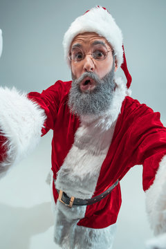 Funny surprised guy with christmas hat posing at studio. New Year Holiday. Christmas, x-mas, winter, gifts concept. Man wearing Santa Claus costume on gray. Copy space. Winter sales.