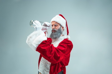 Fototapeta na wymiar Funny guy with christmas hat posing at studio. New Year Holiday. Christmas, x-mas, winter, gifts concept. Man wearing Santa Claus costume on gray. Copy space. Winter sales.