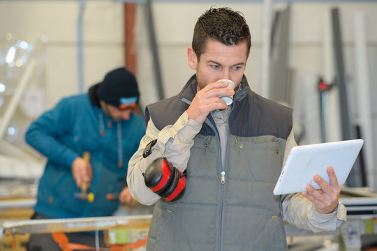 warehouse worker drinking coffee while checking his tablet