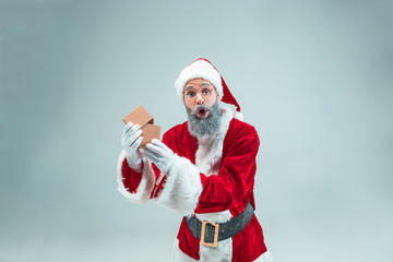 Fototapeta na wymiar Funny guy with christmas hat posing at studio with gift. New Year Holiday. Christmas, x-mas, winter, gifts concept. Man wearing Santa Claus costume on gray. Copy space. Winter sales.
