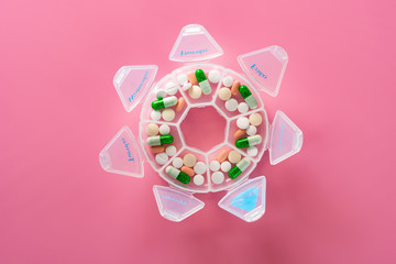 top view daily doses pills in a plastic container on pink background