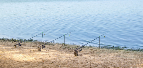 near the blue sea water river stand three fishing rods on the yellow sand fishing
