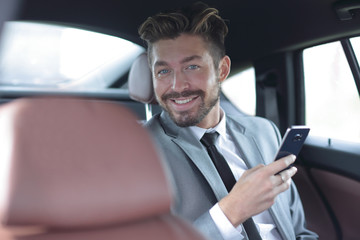 Unsmiling businessman sitting in the back seat in his car