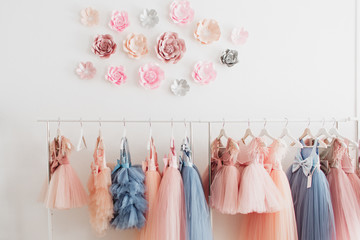 Beautiful dressy lush pink and blue dresses for girls on hangers at the background of white wall....