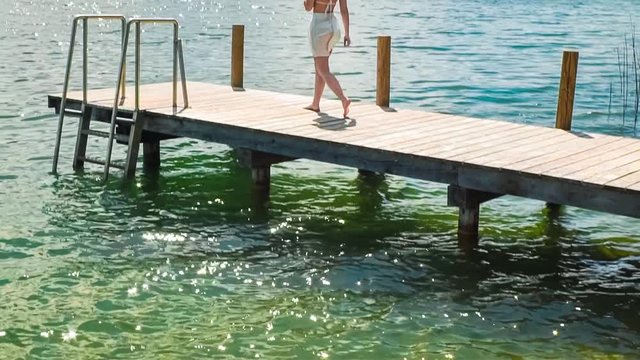 Reveal shot of young woman walking on a dock in Worthersee lake, Austria mountain view windy hair in slow-motion