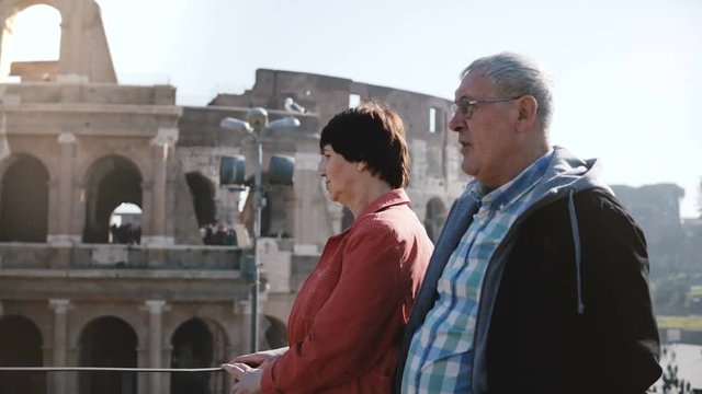 Happy active senior Caucasian tourist couple enjoying the view of famous Coliseum together during trip to Rome, Italy.