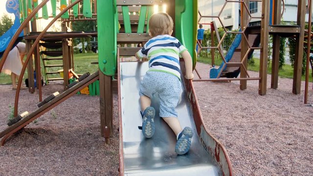 4k video of little toddler boy climbing on metal slide on playground at park