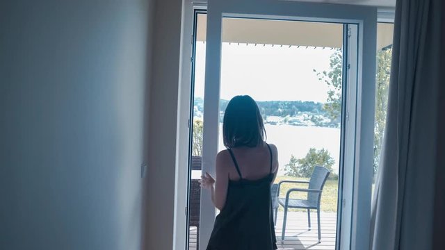 Young woman in underwear open curtains of a hotel, resort in the morning, gets outside and admires the lake view
