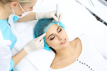 Fototapeta premium Professional beautician doing eyebrow tattoo at woman face. Permanent brow makeup in beauty salon, closeup. Cosmetology treatment
