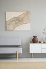 Real photo of modern art poster with cloth hanging on the wall in living room interior with grey...