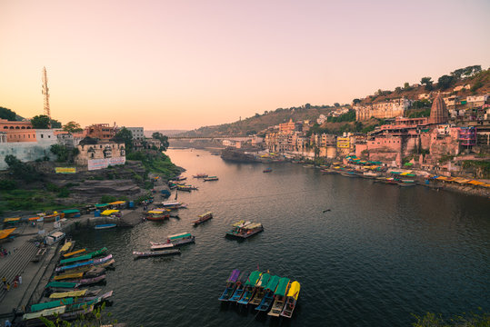 Omkareshwar cityscape, India, sacred hindu temple. Holy Narmada River, boats floating. Travel destination for tourists and pilgrims.