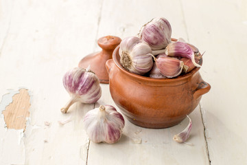   The heads and cloves of fresh garlic in a round clay pot on an old wooden table. 