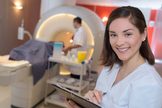 happy female radiologist with colleagues in background by mri machine