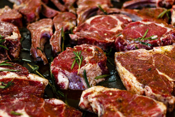 raw pieces of beef steak with rosemary sprigs in a frying pan
