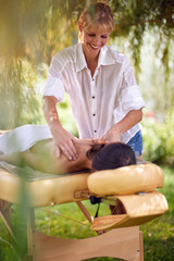 Massage therapy, healthcare concept, woman lying on massage bed receiving a treatment from a masseur in nature.