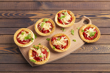 Mini pizza with salami, tomato and cheese on wooden background. Tasty appetizer, tartlet.