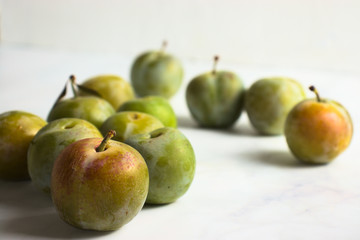 Group of small greengage plums on white marble