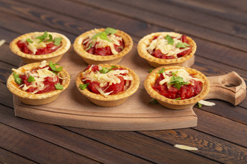 Mini pizza with salami, tomato and cheese on wooden background. Tasty appetizer, tartlet.