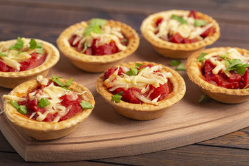 Mini pizza with salami, tomato and cheese on wooden background. Tasty appetizer, tartlet.